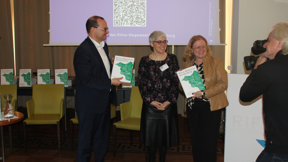 Sophia Becker hands out the climate guide to State Secretaries Friederike Haase and Tobias Dünow.